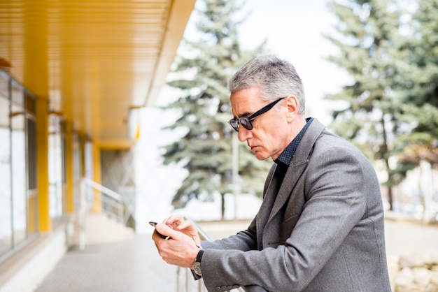 Bezpłatne zdjęcie starszy biznesmen za pomocą telefonu komórkowego na zewnątrz