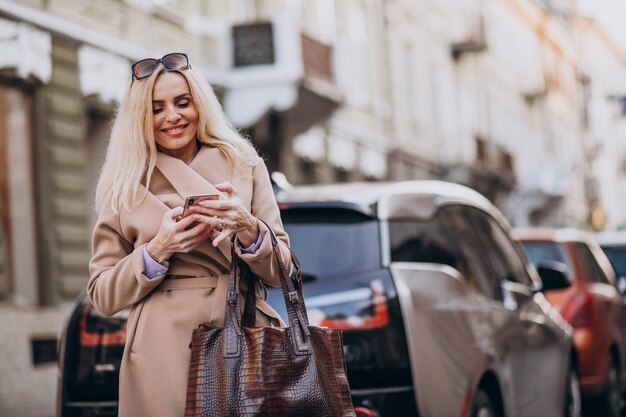 Starszy bizneswoman opowiada na telefonie jej elektrycznym samochodem