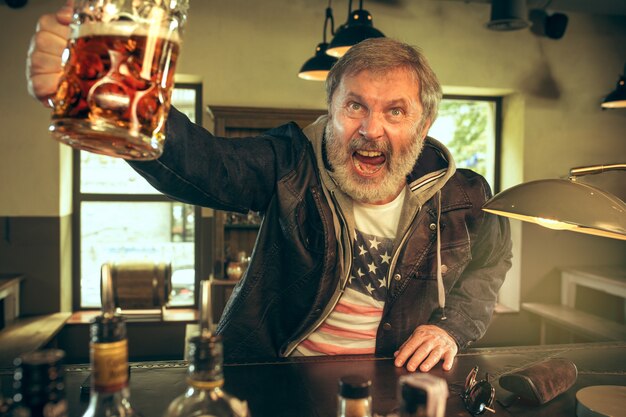 Starszy brodaty mężczyzna pije piwo w pubie