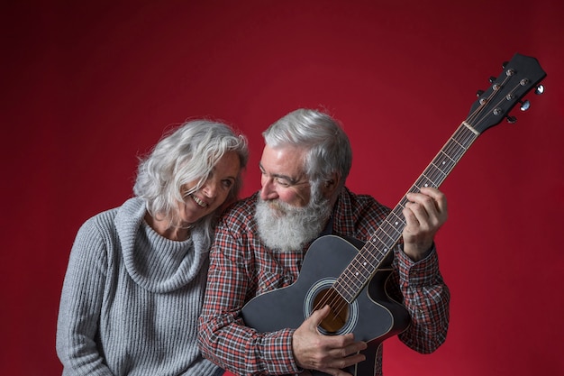 Starszy kobieta siedzi w pobliżu jej mąż gra na gitarze na czerwonym tle