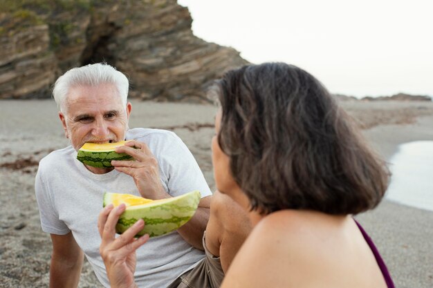 Starszy mężczyzna i kobieta jedzą arbuza na plaży