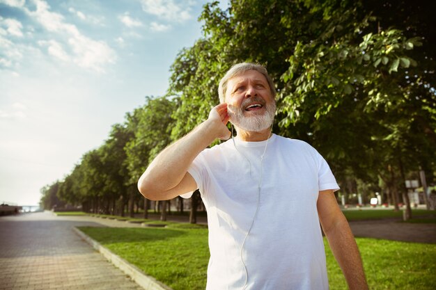 Starszy mężczyzna jako biegacz z trackerem fitness na ulicy miasta. Kaukaski mężczyzna model za pomocą gadżetów podczas joggingu i treningu cardio w letni poranek. Zdrowy styl życia, sport, koncepcja aktywności.