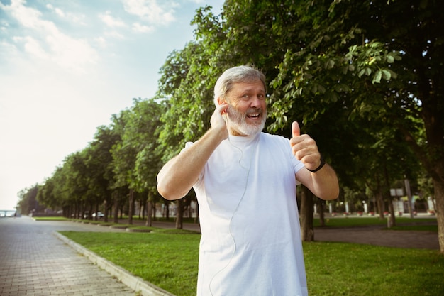 Starszy mężczyzna jako biegacz z trackerem fitness na ulicy miasta. Kaukaski mężczyzna model za pomocą gadżetów podczas joggingu i treningu cardio w letni poranek. Zdrowy styl życia, sport, koncepcja aktywności.