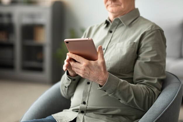 Starszy mężczyzna korzystający z tabletu siedzącego na kanapie w salonie