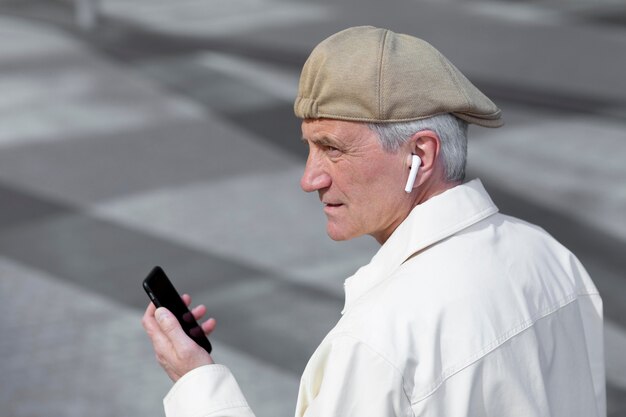 Bezpłatne zdjęcie starszy mężczyzna na zewnątrz w mieście za pomocą smartfona z wkładkami dousznymi