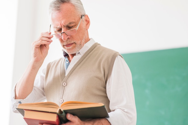 Bezpłatne zdjęcie starszy mężczyzna profesor czytanie książki podczas korygowania okularów