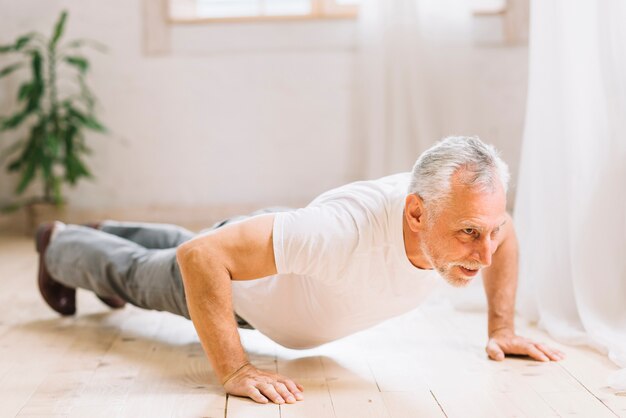 Starszy mężczyzna robi ćwiczenia pushup na drewnianej podłodze