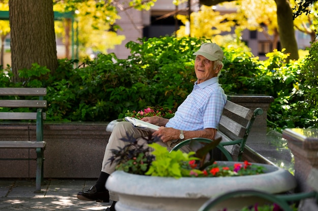 Bezpłatne zdjęcie starszy mężczyzna siedzi na ławce na zewnątrz i czyta książkę