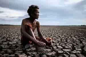 Bezpłatne zdjęcie starszy mężczyzna siedział, obejmując kolana zgiętymi na suchej ziemi, i patrzył w niebo