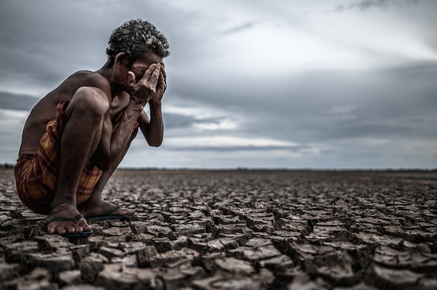 Bezpłatne zdjęcie starszy mężczyzna siedział zgięty w kolanach na suchej ziemi i ręce zamknięte na twarzy, globalne ocieplenie