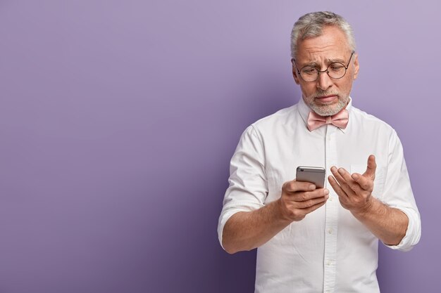 Starszy mężczyzna w białej koszuli i różowej muszce trzymając telefon