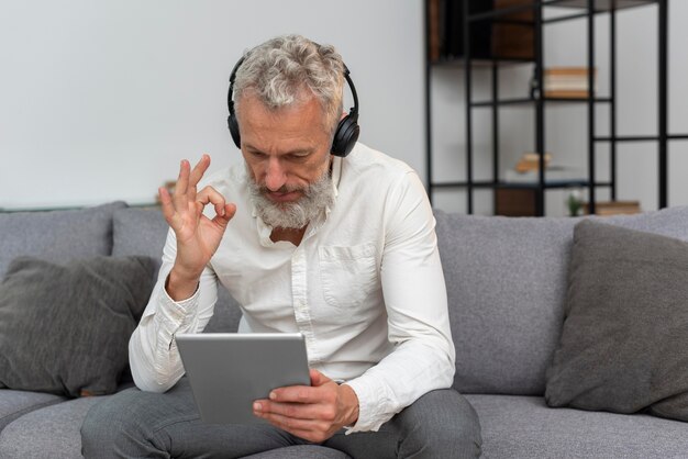 Starszy mężczyzna w domu na kanapie podczas rozmowy wideo na tablecie i noszenia słuchawek