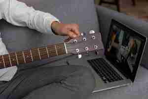 Bezpłatne zdjęcie starszy mężczyzna w domu na kanapie za pomocą laptopa do nauki lekcji gry na gitarze