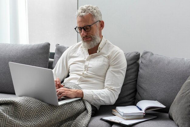 Starszy mężczyzna w domu studiuje na kanapie za pomocą laptopa