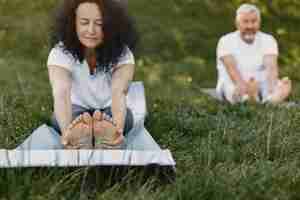 Bezpłatne zdjęcie starszy para robi joga na świeżym powietrzu. rozciąganie w parku podczas wschodu słońca. brunetka w białej koszulce.