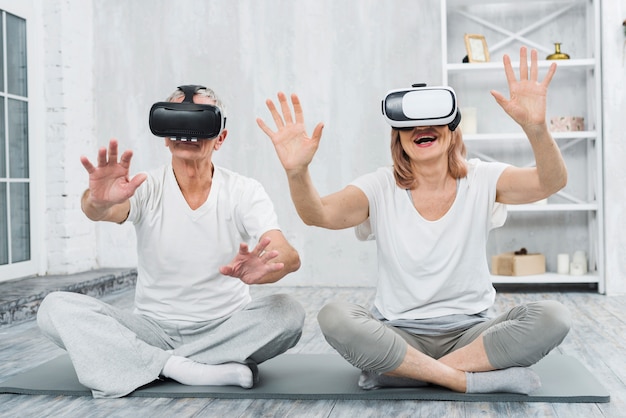 Bezpłatne zdjęcie starszy starsza para siedzi na szarej macie zabawy z okularami wirtualnej rzeczywistości