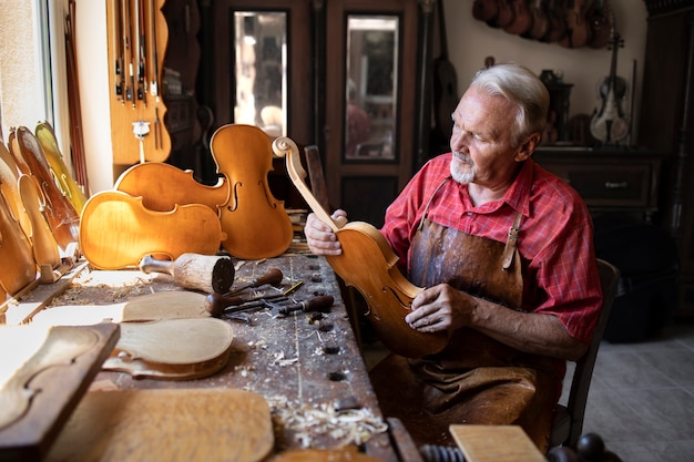 Starszy stolarz montujący elementy instrumentu skrzypcowego w swoim warsztacie stolarskim