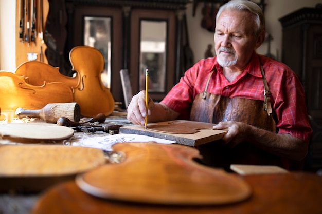 Bezpłatne zdjęcie starszy stolarz rzemieślnik wykonujący instrument muzyczny skrzypce w swoim staromodnym warsztacie stolarskim