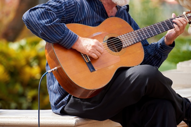 Stary człowiek bawić się gitarę outside w ogródzie