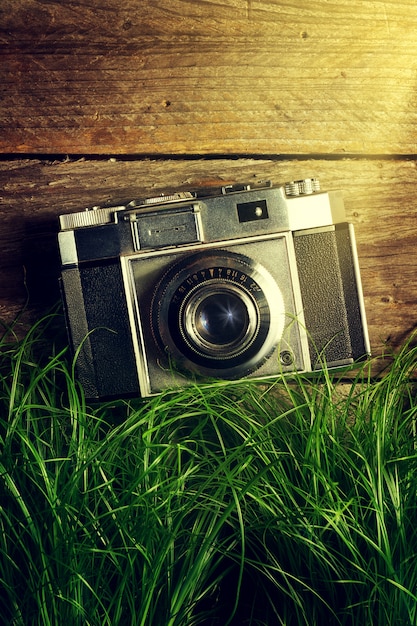 Bezpłatne zdjęcie stary vintage kamery w zielonej trawie z belek światła na drewnianym tle. widok z góry.