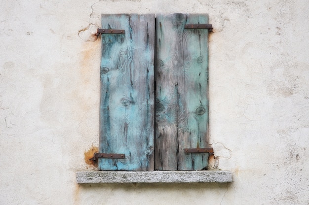 Stary wyblakły mur z niebieskimi zardzewiałymi drewnianymi okiennicami