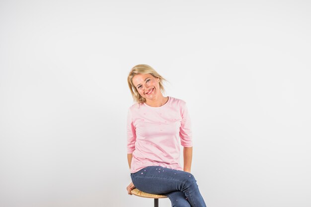 Starzejąca się uśmiechnięta kobieta w różanej bluzce na stolec