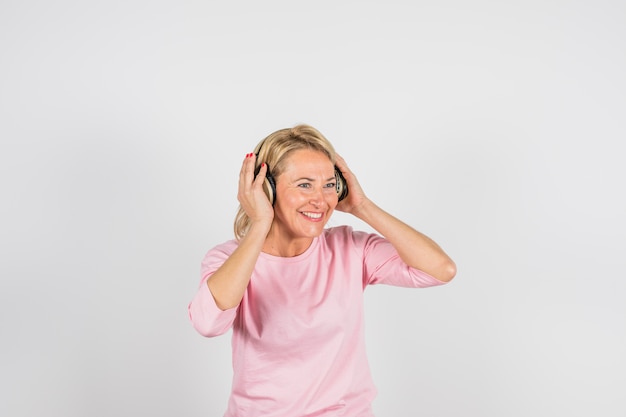 Starzejąca się uśmiechnięta kobieta w różanej bluzce z hełmofonami