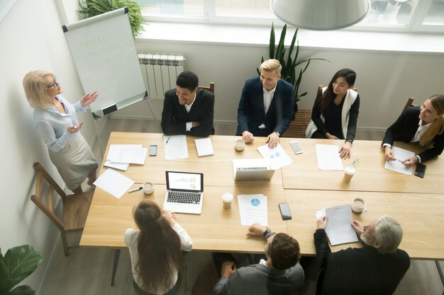 Starzejący się starszy bizneswoman daje prezentaci przy wielorasowym grupowym biurowym spotkaniem