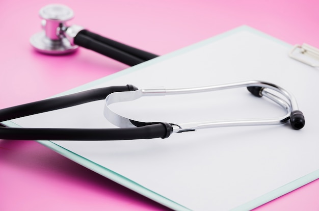 Bezpłatne zdjęcie stetoskop na białym papierze nad schowkiem przeciw różowemu tłu
