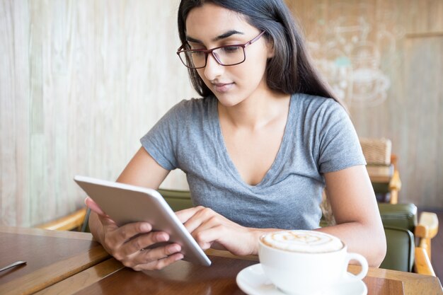 Stężony student indyjski za pomocą tabletu w kawiarni