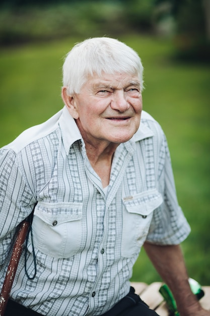 Stock Photo Portret Starego Mężczyzny Rasy Kaukaskiej W Kratkę Koszulę Z Dwiema Kieszeniami Na Klatce Piersiowej Z Kulą Pod Pachą Sittingon ławce Na Zewnątrz I Uśmiecha Się Do Kamery.