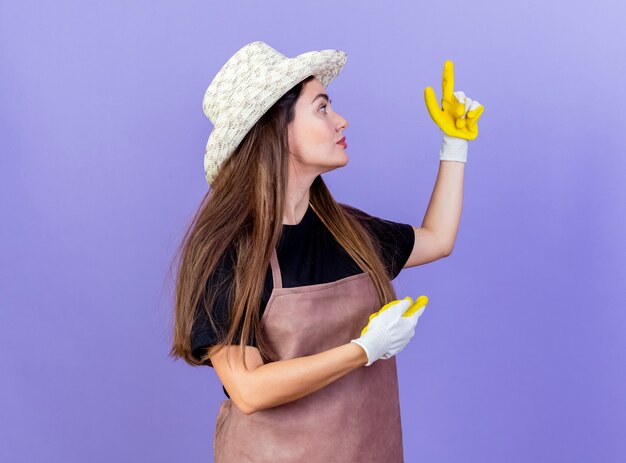 Stojąc w widoku profilu piękna dziewczyna ogrodnik w mundurze na sobie kapelusz ogrodniczy i rękawiczki punkty po różnych stronach odizolowane na niebiesko