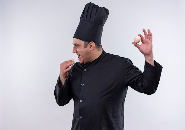 Stojący w widoku profilu w średnim wieku kucharz mężczyzna w mundurze szefa kuchni trzymając jajka