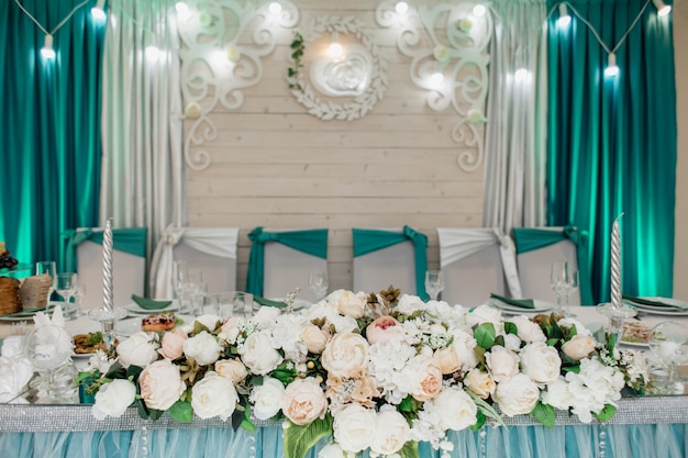 Stół weselny dla pana młodego i panny młodej, ozdobiony kompozycją kwiatową wykonaną z białych róż, w odcieniach seledynu