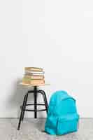 Bezpłatne zdjęcie stos książek na stołku krzesło z tornister niebieski na podłodze