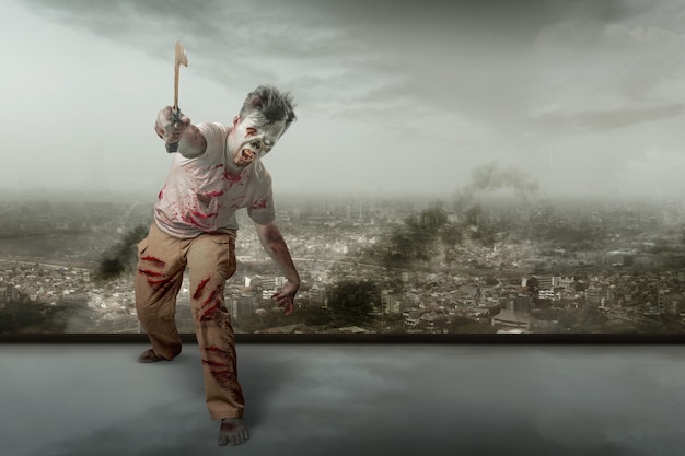 Straszny zombie z krwią i raną na ciele trzymający sierp chodzący na tle zrujnowanego miasta