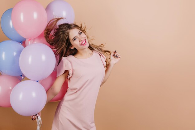Strzał studio całkiem biała dziewczyna nosi różową sukienkę taniec z balonami. Wewnątrz zdjęcie emocjonalnej europejskiej damy pozującej przed przyjęciem urodzinowym.