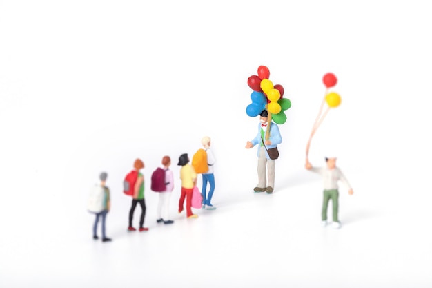 Bezpłatne zdjęcie strzał zbliżenie miniaturowych figurek uczniów zbliżających się do mężczyzny trzymającego balony