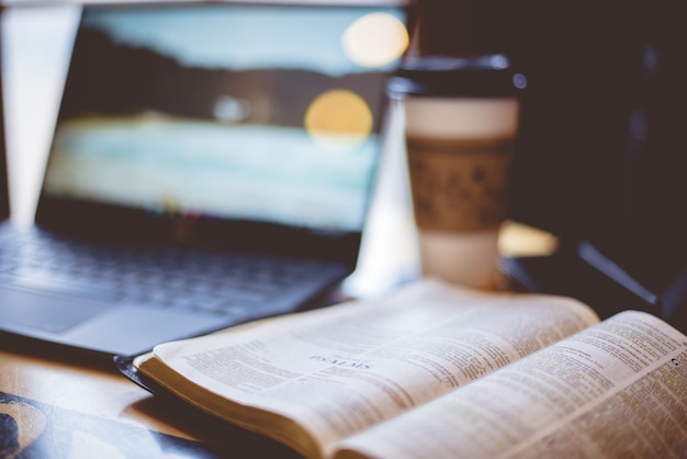 Strzał zbliżenie otwartej Biblii z niewyraźnym laptopem i kawą