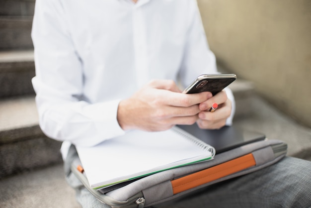 Student collegu używa jego telefon i siedzący na schodkach