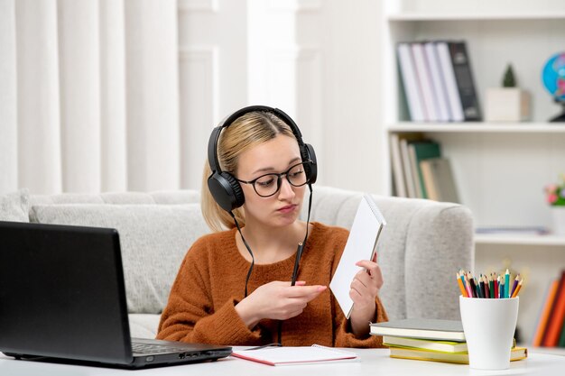 Student online ładna dziewczyna w okularach i swetrze studiuje na komputerze pokazując notatki