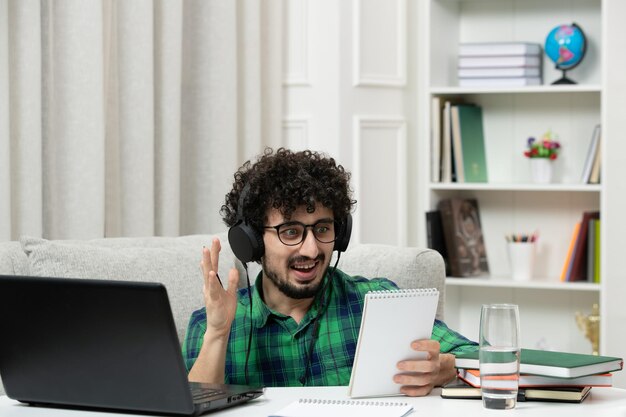 Student online ładny młody facet studiujący na komputerze w okularach w zielonej koszuli uśmiechający się notatki do czytania
