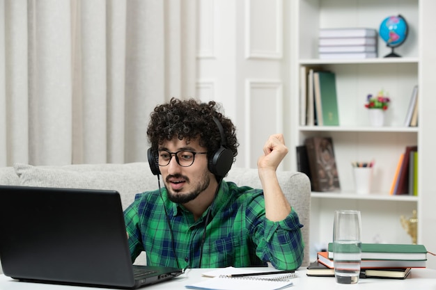 Student online ładny młody facet studiuje na komputerze w okularach w zielonej koszuli ciężko pracuje