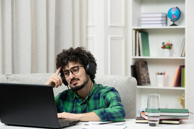 Student online ładny młody facet studiuje na komputerze w okularach w zielonej koszuli, myśląc