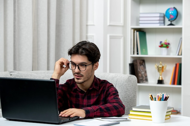 Student online młody facet w kraciastej koszuli w okularach studiuje na komputerze słuchając wykładu