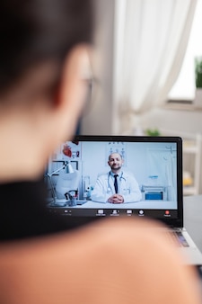 Student pracuje z domu lekarza prowadzącego wideorozmowy na laptopie. widok przez ramię freelancera podczas rozmowy wideo online konsultacji medycznej. lekarz udziela porad zdrowotnych przez kamerę internetową.