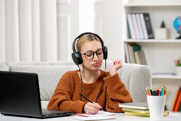 Studentka online ładna dziewczyna w okularach i swetrze studiuje na komputerze, zdejmując notatki