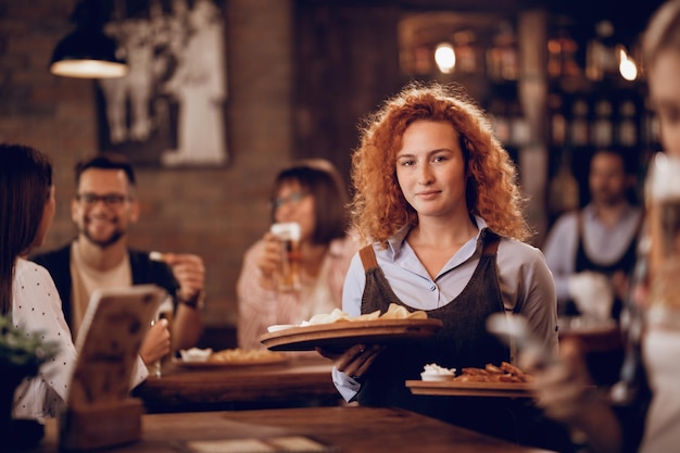Bezpłatne zdjęcie studentka pracująca w niepełnym wymiarze godzin jako kelnerka i serwująca jedzenie gościom w pubie