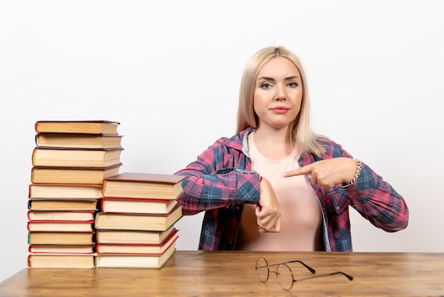 Bezpłatne zdjęcie studentka siedzi z książkami, wskazując na jej nadgarstek na białym tle