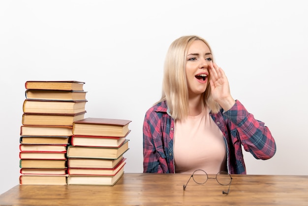 Bezpłatne zdjęcie studentka siedzi z książkami wzywając kogoś na biały